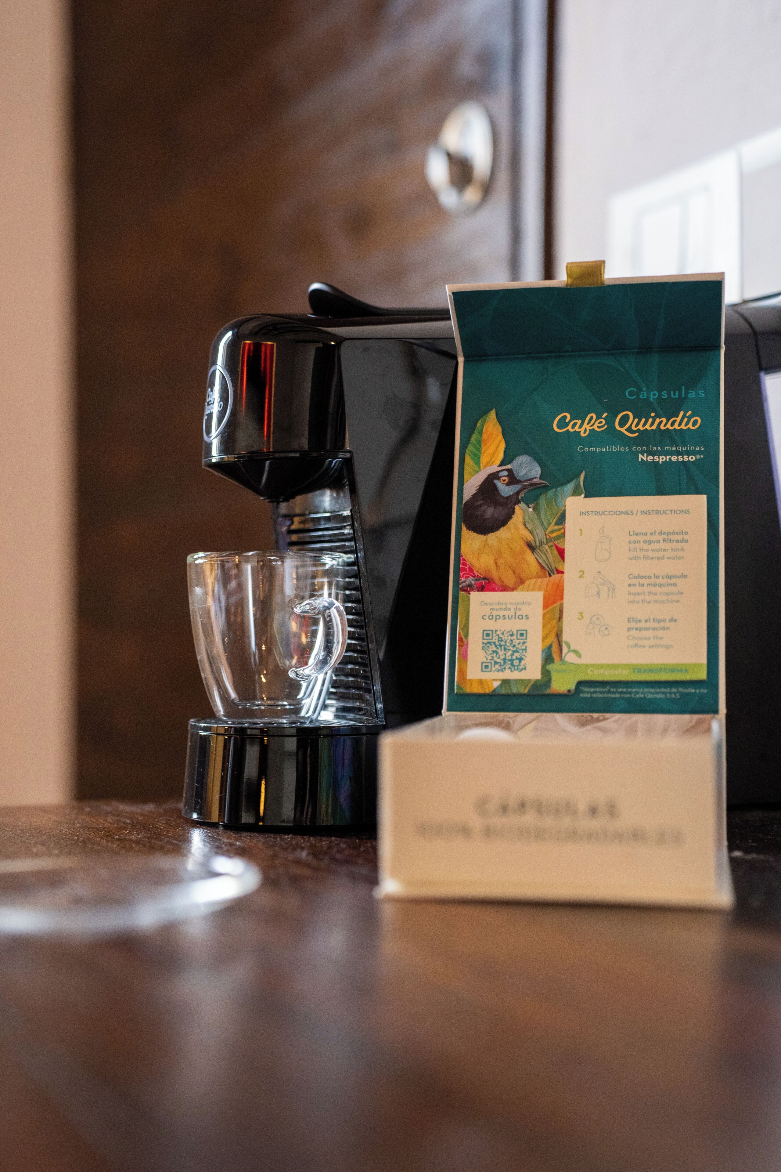Una cafetera, una taza de vidrio y un paquete de cápsulas de café sobre una encimera.