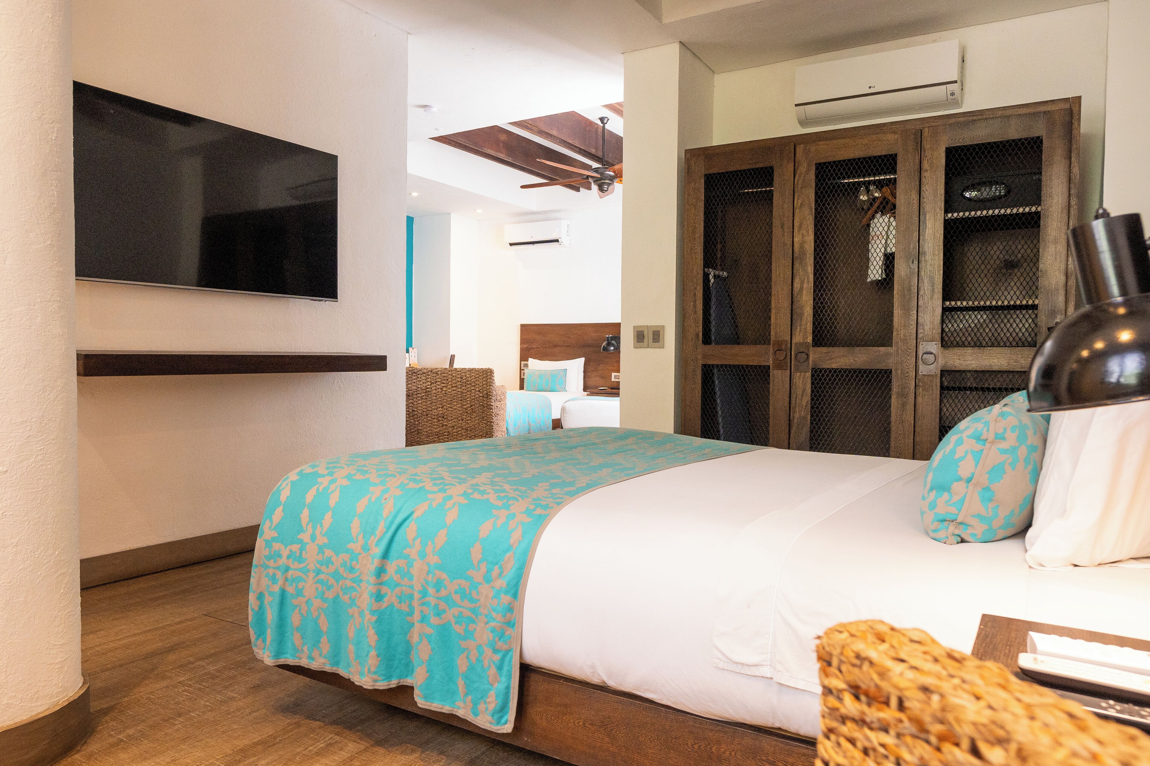 A hotel room with a bed, a television, a wardrobe, and an air conditioning unit.