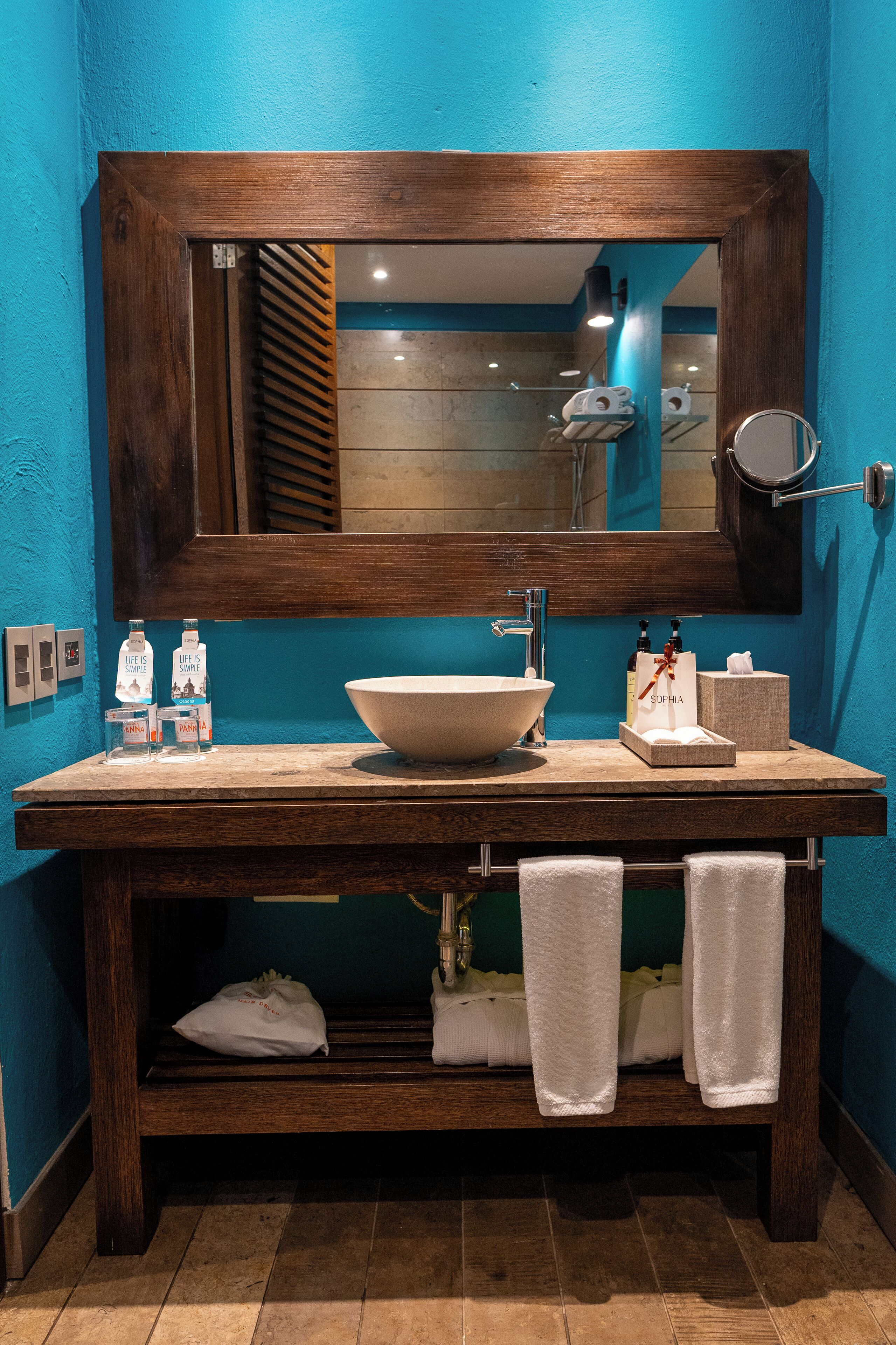 A bathroom with a wooden vanity, a large sink, and a mirror above it. There are towels hanging on a rack below the vanity.