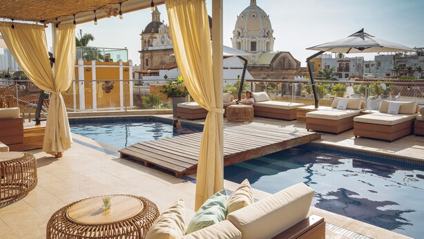 Area piscina sul tetto con sedute lounge, una piscina e vista su un edificio storico.