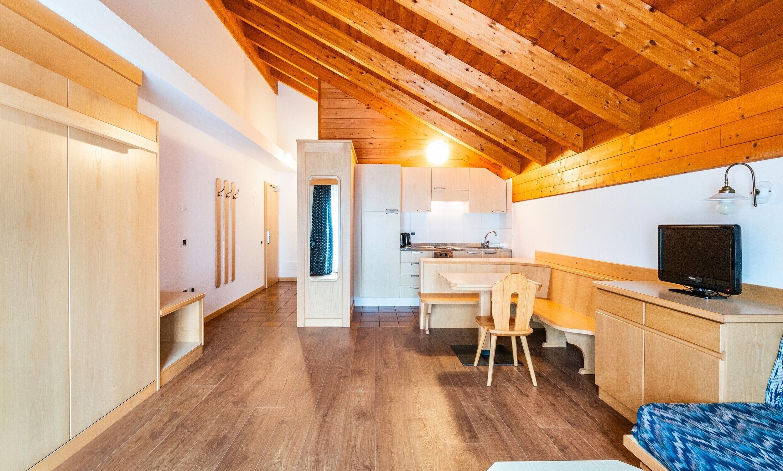 Una cocina compacta con zona de comedor, vigas de techo de madera y un televisor sobre un mueble de madera.
