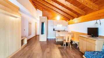Une cuisine compacte avec un coin repas, des poutres apparentes en bois au plafond et un téléviseur posé sur un meuble en bois.