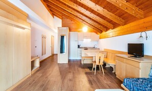 A compact kitchen with a dining area, wooden ceiling beams, and a television on a wooden cabinet.