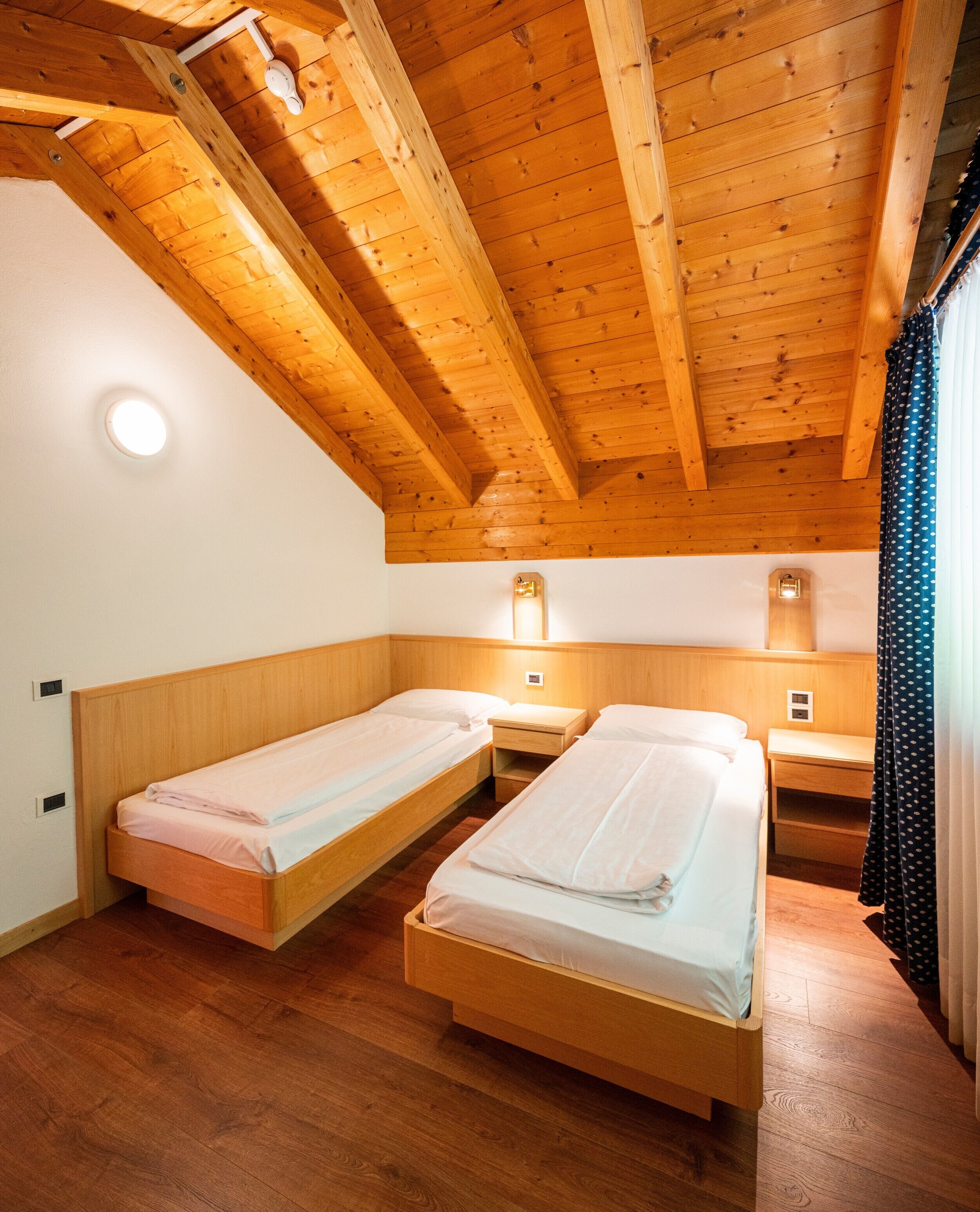 A room with two single beds, wooden ceiling beams, and a small wall-mounted light fixture.