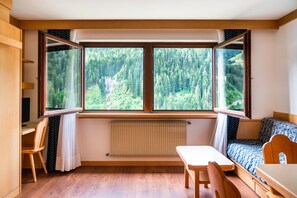 A room with a large window, a bed, a table, and a chair. - Apartments Boè (Santa Cristina Val Gardena)