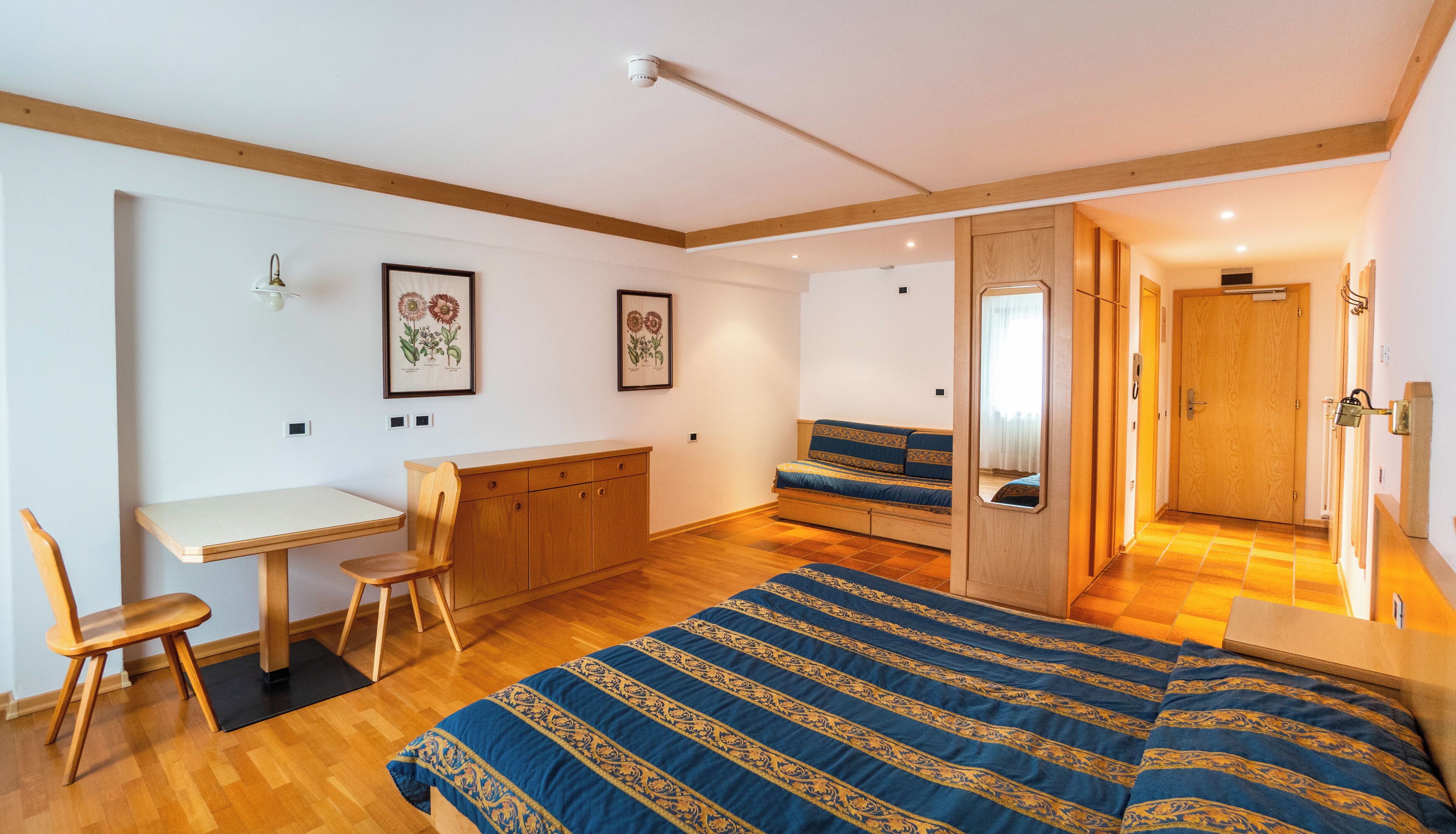 A bedroom with a bed, a desk, a chair, a wardrobe, and a mirror.