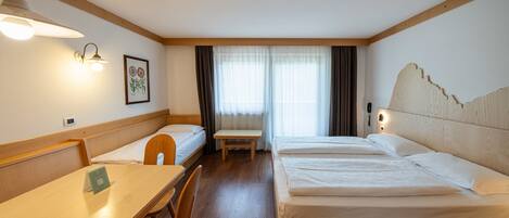 Une chambre d’hôtel avec une tête de lit en bois, un bureau avec une chaise, un lit et une fenêtre avec des rideaux.