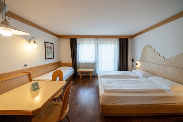 Una habitación de hotel con cabecera de madera, un escritorio con silla, una cama y una ventana con cortinas.