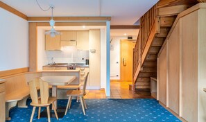 A compact kitchen with a dining area, wooden staircase, and a blue patterned carpet. - Apartments Boè (Santa Cristina Val Gardena)