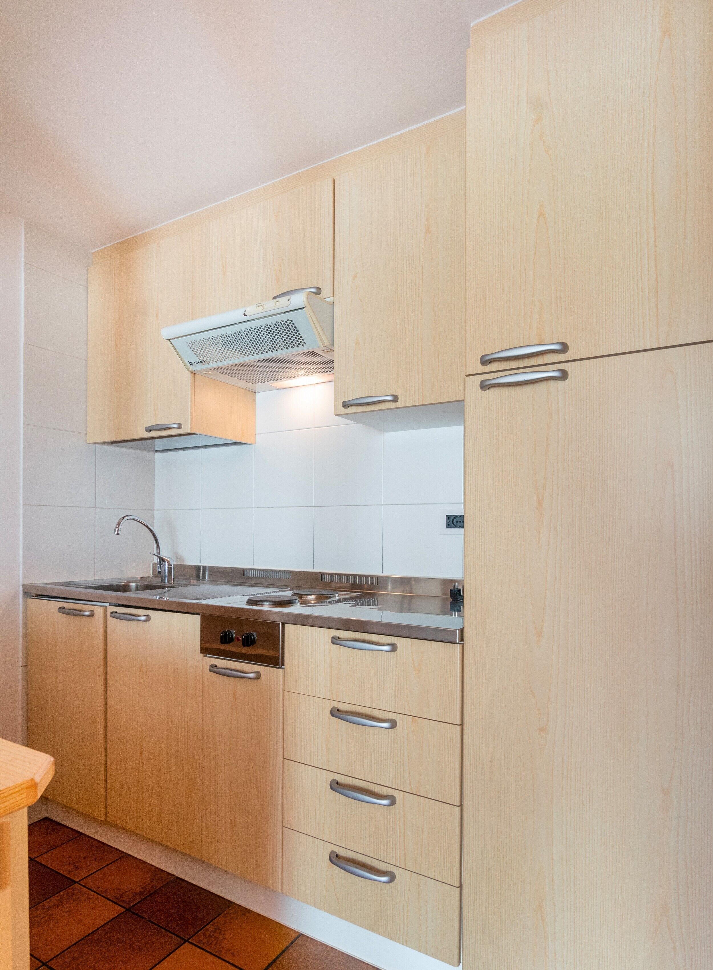 A kitchen with wooden cabinets, a stainless steel sink, and a range hood.