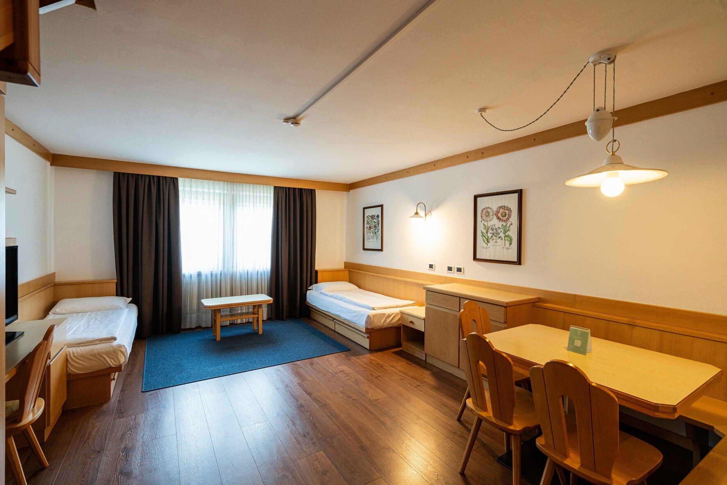 Ein Hotelzimmer mit einem Bett, einem Schreibtisch, einem Sessel, einem kleinen Tisch, einer Bank und einem Esstisch mit Stühlen.