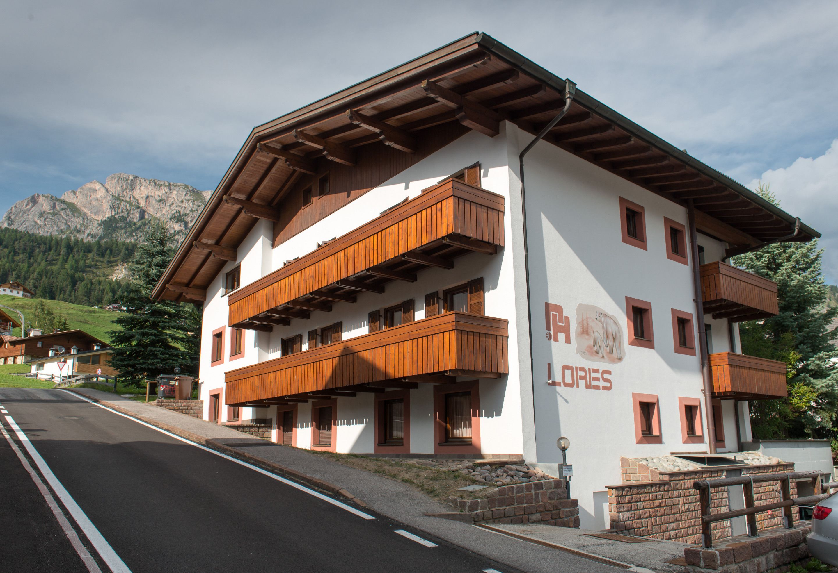 A two-story hotel with wooden balconies and a mountain backdrop.