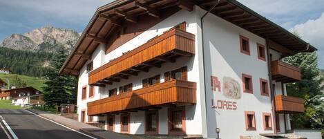 Un hotel de dos pisos con balcones de madera y montañas al fondo.