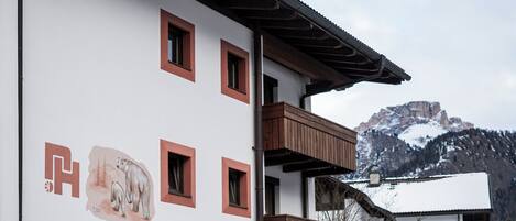 Un edificio con varias ventanas y balcones, un letrero con un logo y texto, y un paisaje montañoso de fondo.