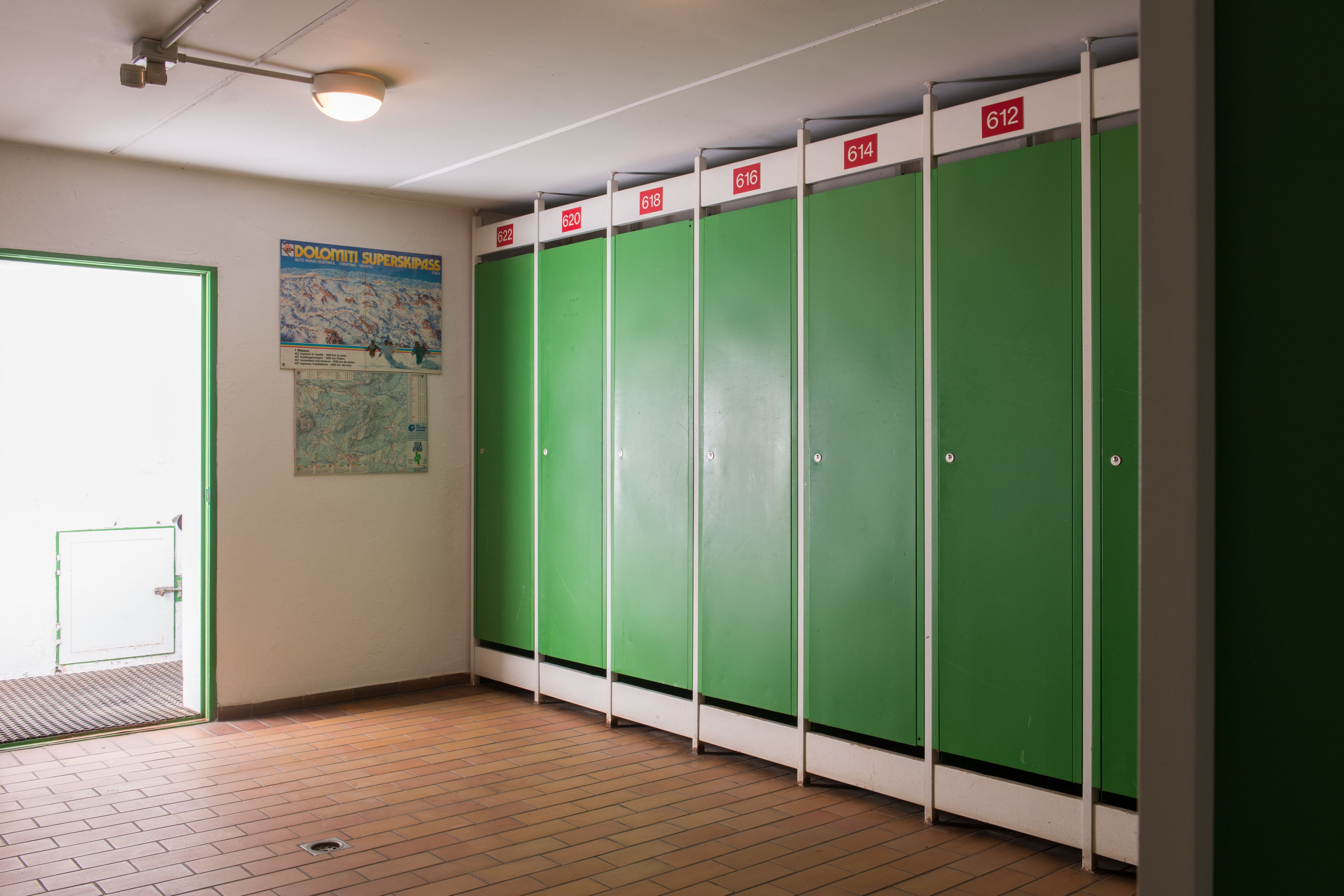 A restroom with green lockers numbered 620 to 614, a door with a green frame, and a poster on the wall.