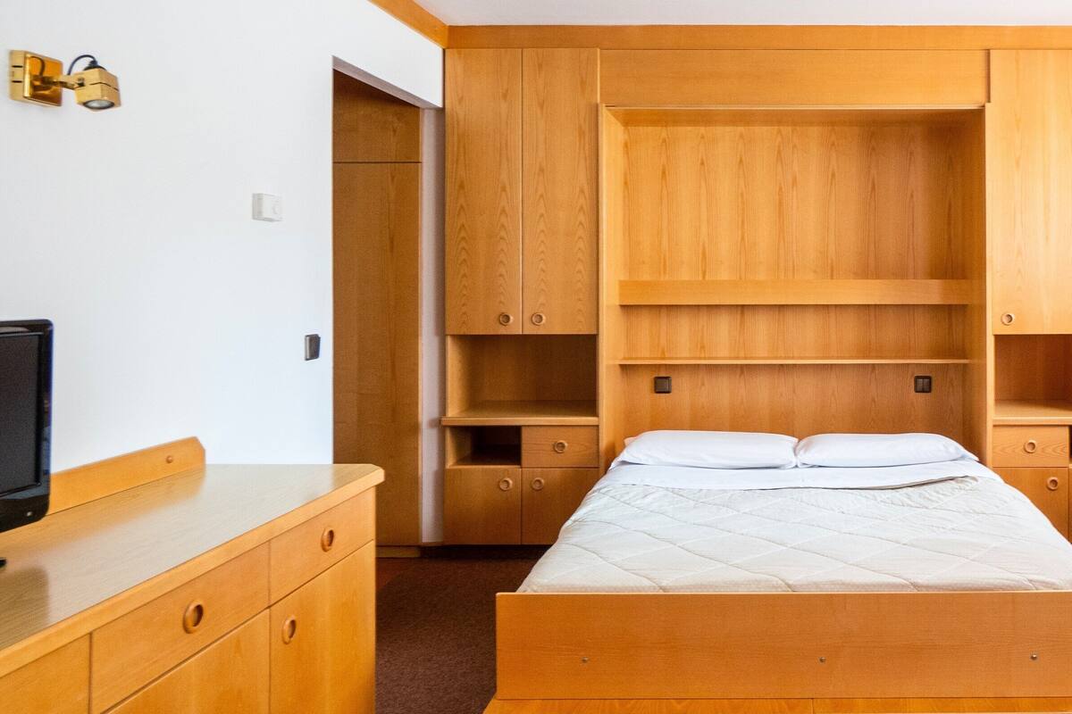 A bedroom with a bed, wooden wardrobe, and a television on a stand.