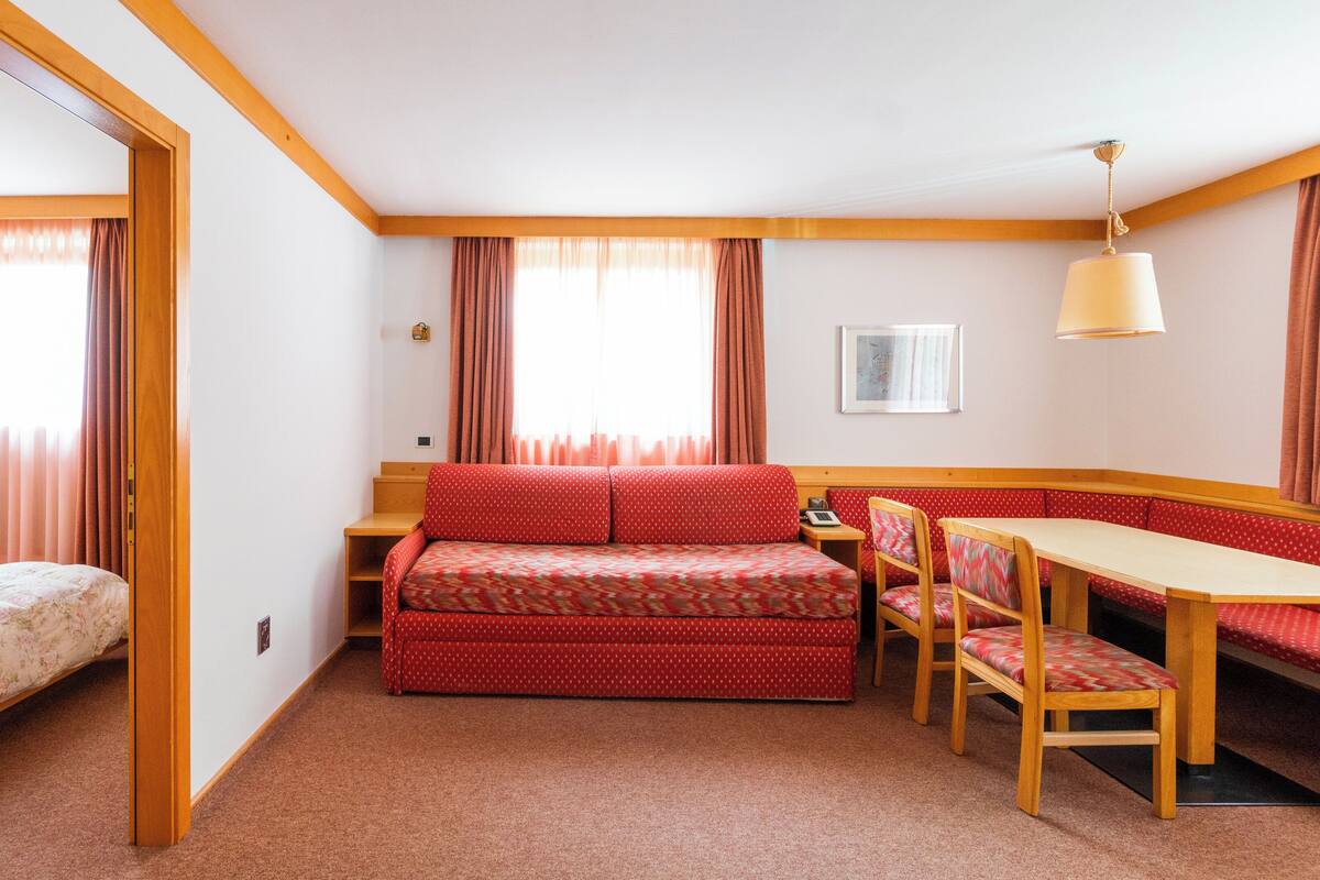 A compact room with a bed, a sofa, a dining table, and chairs.