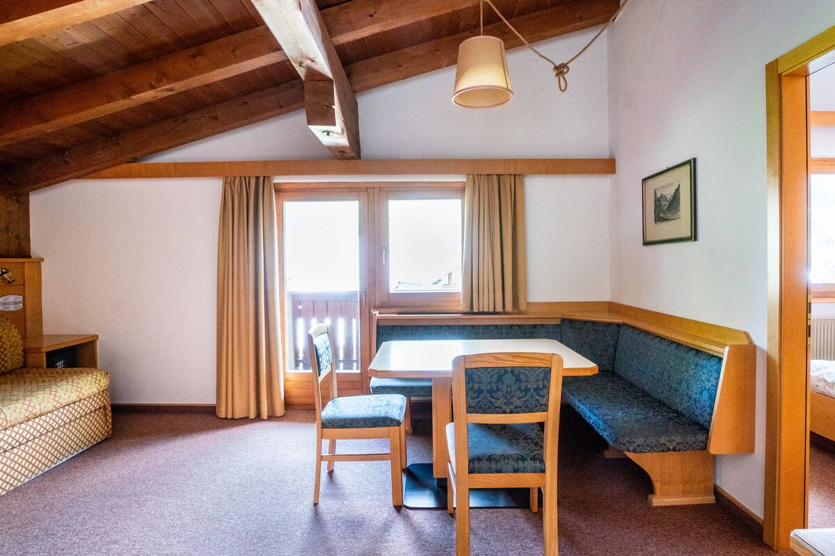 A cozy room with a wooden ceiling, a dining table with chairs, a sofa, and a bed.