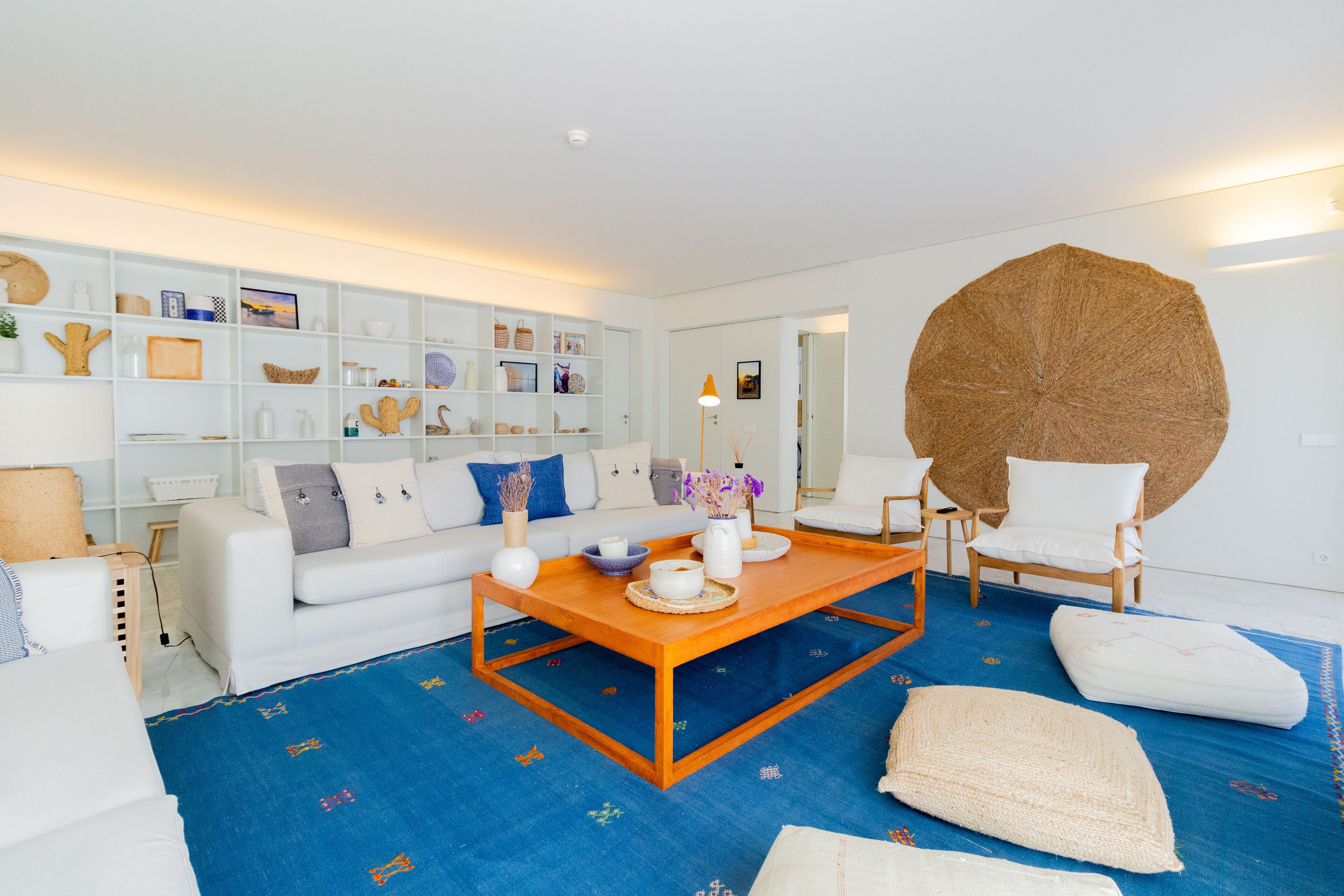 A modern living room with a white sofa, a wooden coffee table, and a large woven rug.