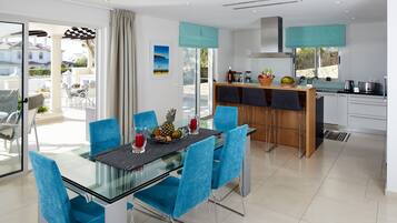 Cocina moderna con comedor, que incluye una mesa de vidrio y sillas azules, una isla de cocina y vistas al exterior.