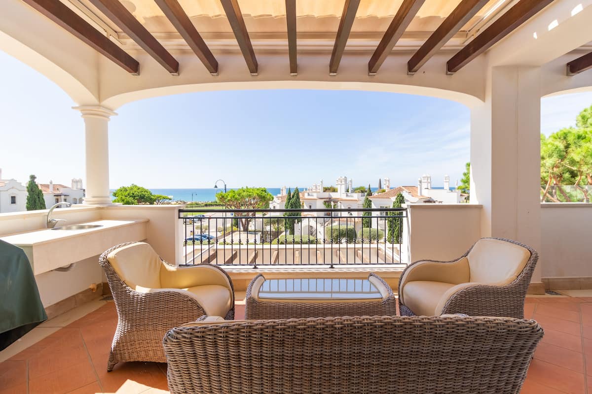 A balcony with wicker furniture, a view of the sea, and a tiled floor.