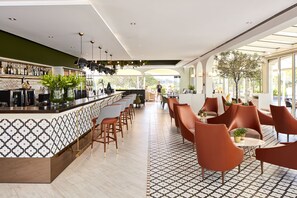 Un área de bar moderna con pared estampada, taburetes y un espacio de asientos con sillas naranjas y alfombra con diseño.