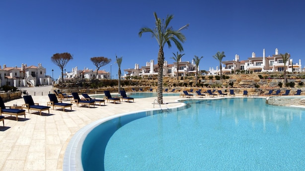 A pool area with lounge chairs and palm trees, surrounded by buildings with Mediterranean architecture. - Dunas Douradas Beach Club (Loulé)
