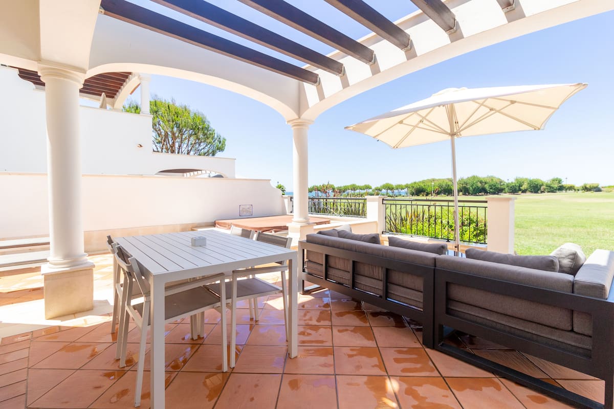 An outdoor patio with a white table and chairs, a grey sofa, and a large umbrella.