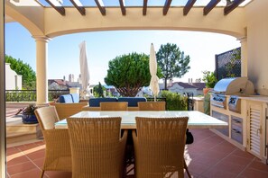 An outdoor patio with wicker furniture, a glass-top table, and a barbecue grill. - Dunas Douradas Beach Club (Loulé)