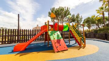 A playground with a slide, climbing wall, and a fenced area.