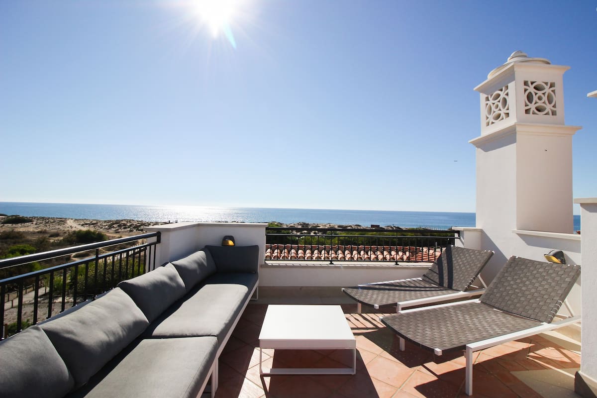 A terrace with a sofa, two lounge chairs, and a table.