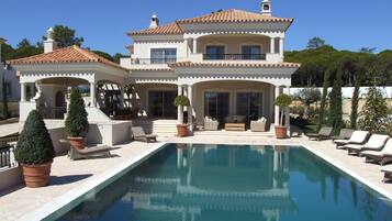 A two-story house with a swimming pool, outdoor seating, and a garden.