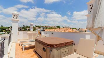 A rooftop terrace with a hot tub, lounge chairs, and a view of the cityscape.