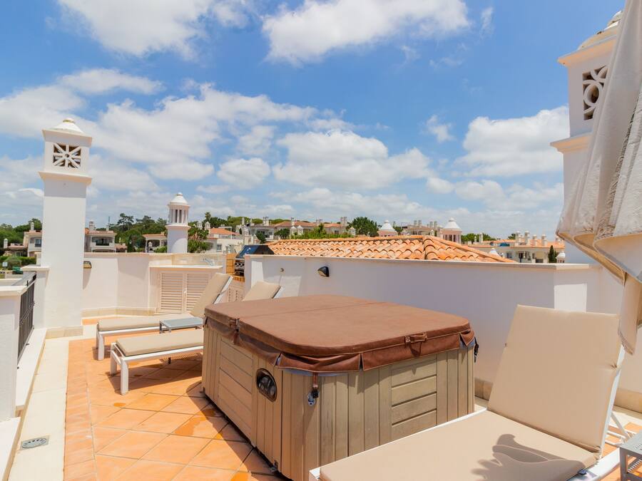 Een dakterras met een jacuzzi, lounge stoelen en uitzicht op de stad.