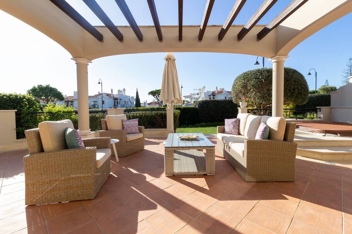 An outdoor patio area with wicker furniture, a tiled floor, and a pergola structure.