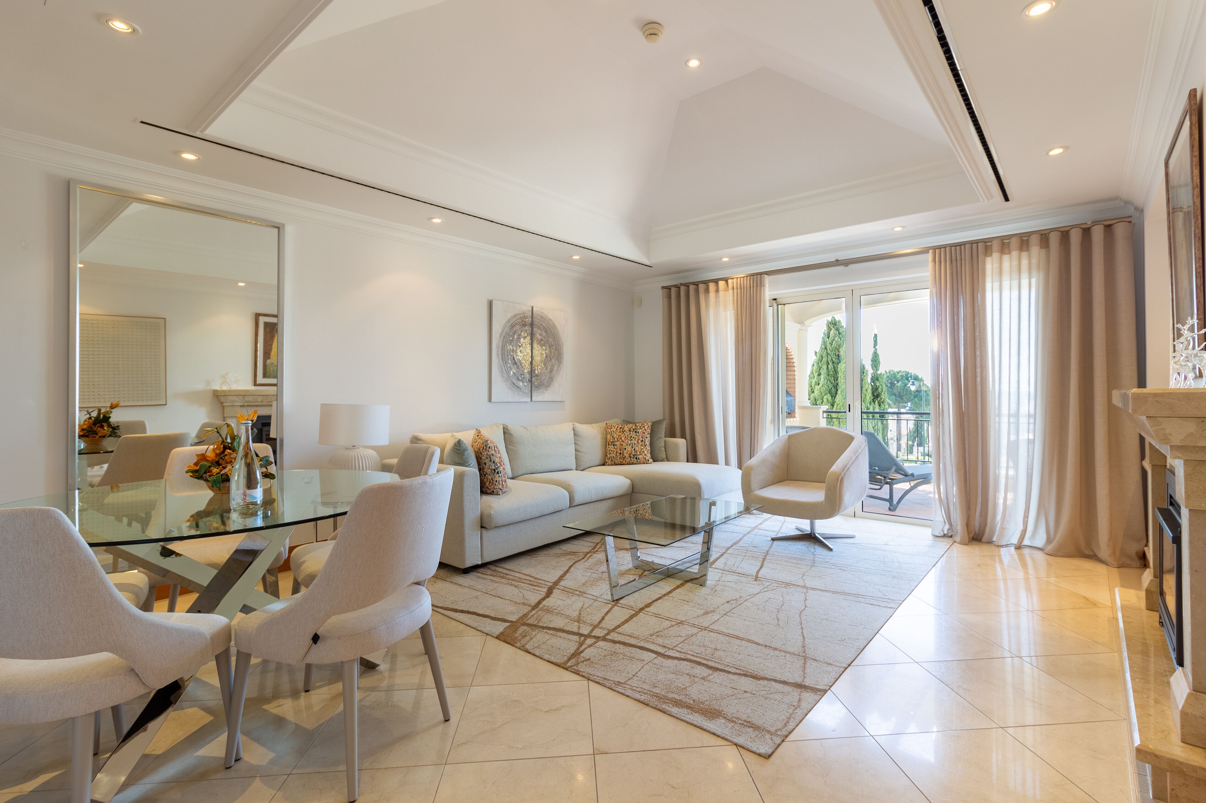A modern living room with a glass coffee table, white sofas, and a glass dining table.