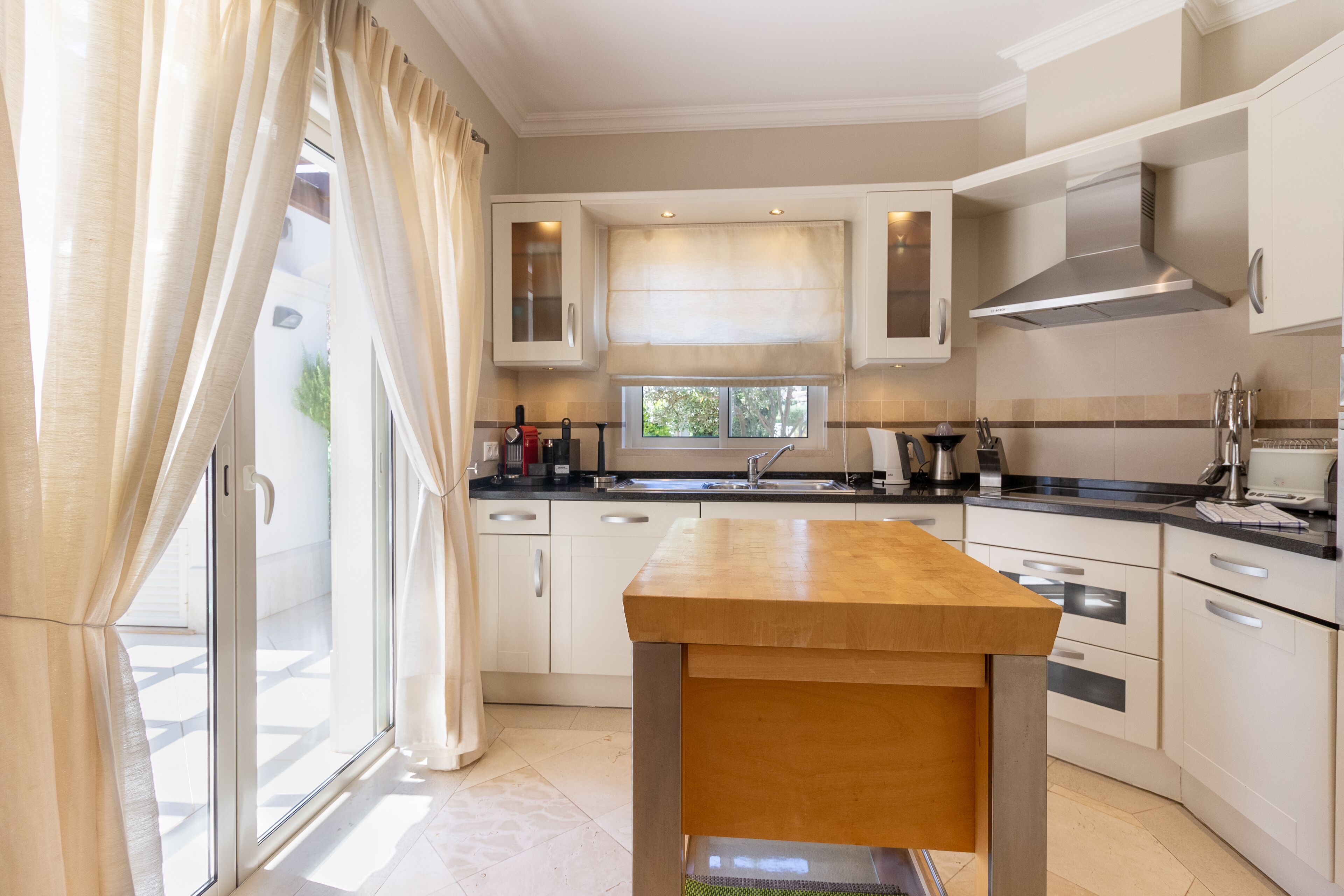 A modern kitchen with a wooden table, white cabinets, and a large window.
