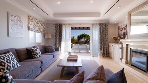 A modern living room with a sofa, a coffee table, and a fireplace. There is a view of the outdoors through a large window. - Dunas Douradas Beach Club (Loulé)
