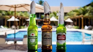 Three bottles of beer in front of a pool with umbrellas and lounge chairs in the background. - Tabaobí Smart Hotel (Ipojuca)