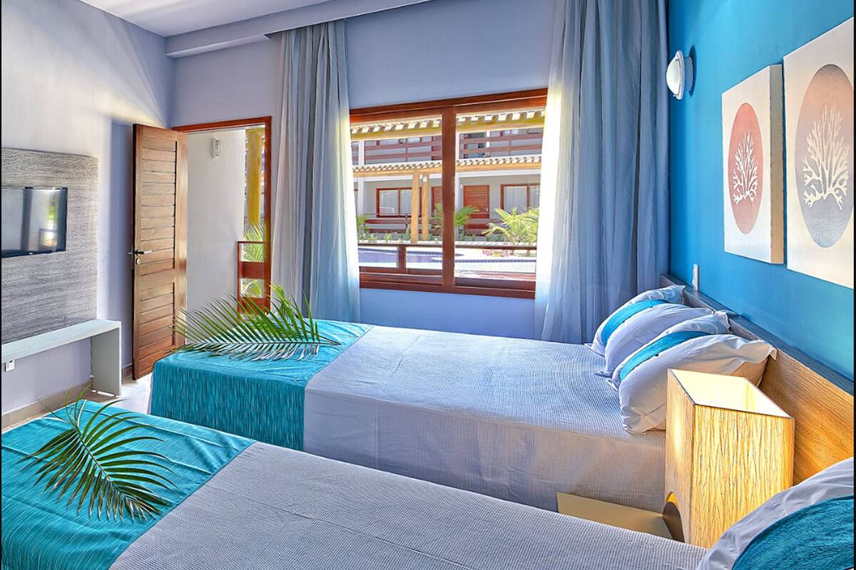 Une chambre d’hôtel avec deux lits, une fenêtre donnant sur un immeuble et un mur orné de tableaux encadrés.
