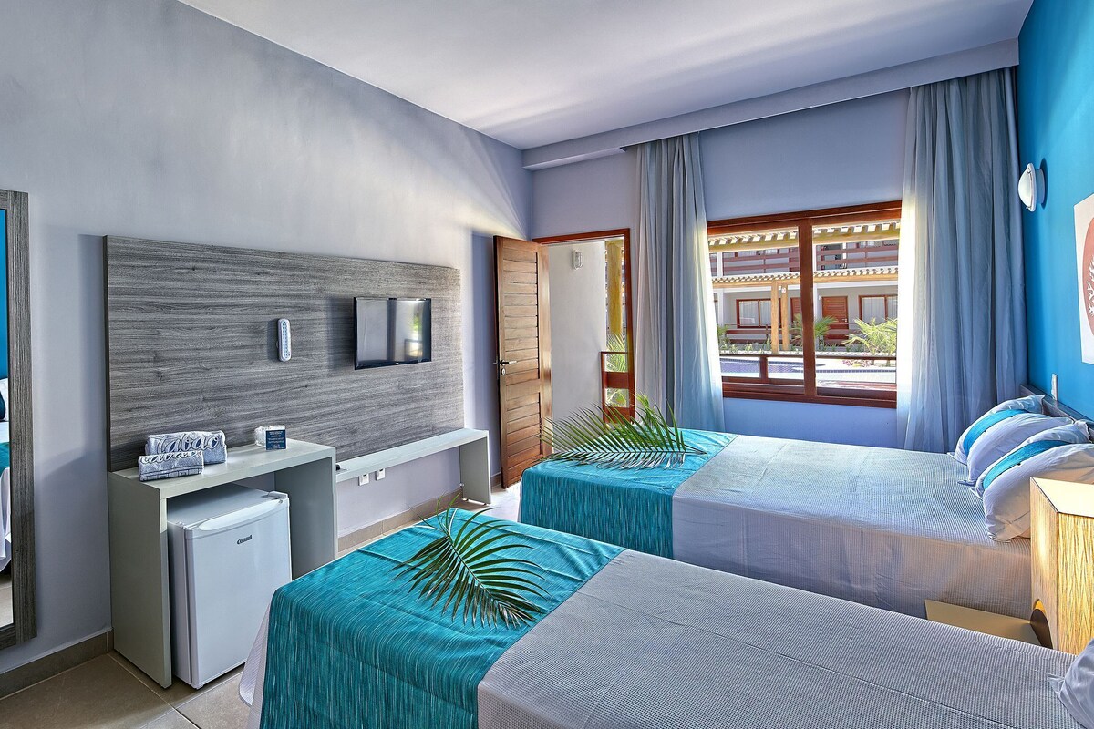 A hotel room with two beds, a small desk, a mirror, and a view of the outside.