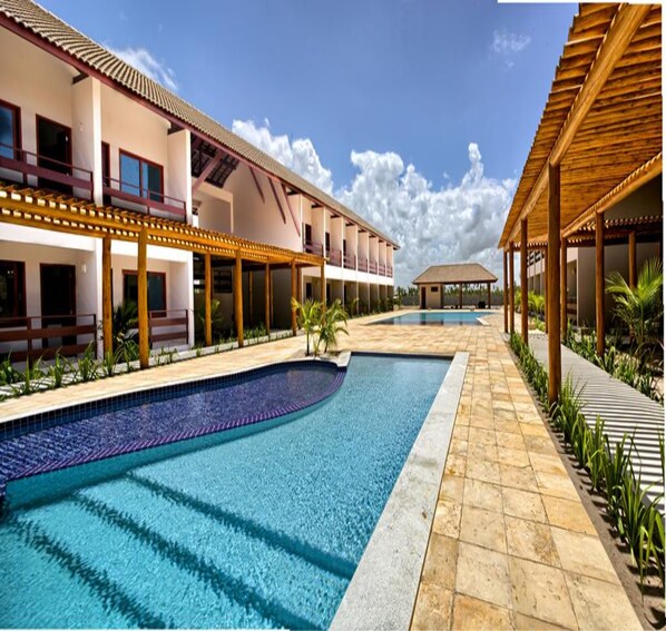 A swimming pool with a curved design, surrounded by a covered walkway and a building with balconies. - Tabaobí Smart Hotel (Ipojuca)