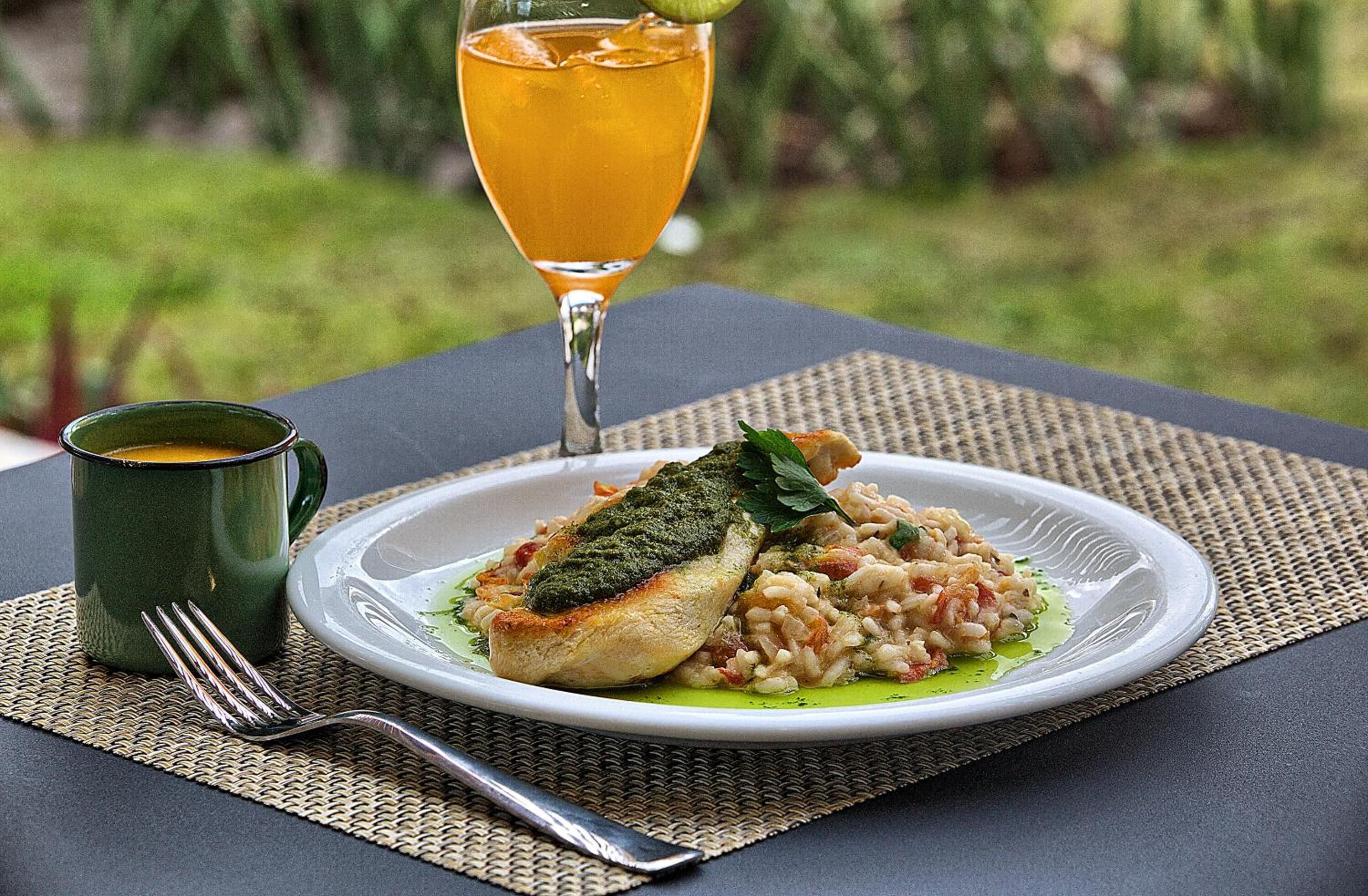 Ein Teller Essen mit grüner Soße, ein Glas Orangensaft und eine grüne Tasse auf einem Tisch mit Untersetzer.