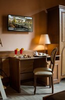 Una habitación de hotel con un escritorio de madera, una silla, un televisor montado en la pared y una lámpara.