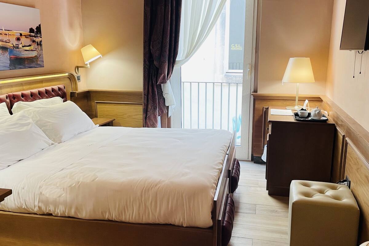 A hotel room with a bed, bedside tables, a desk, a chair, a lamp, and a painting on the wall.