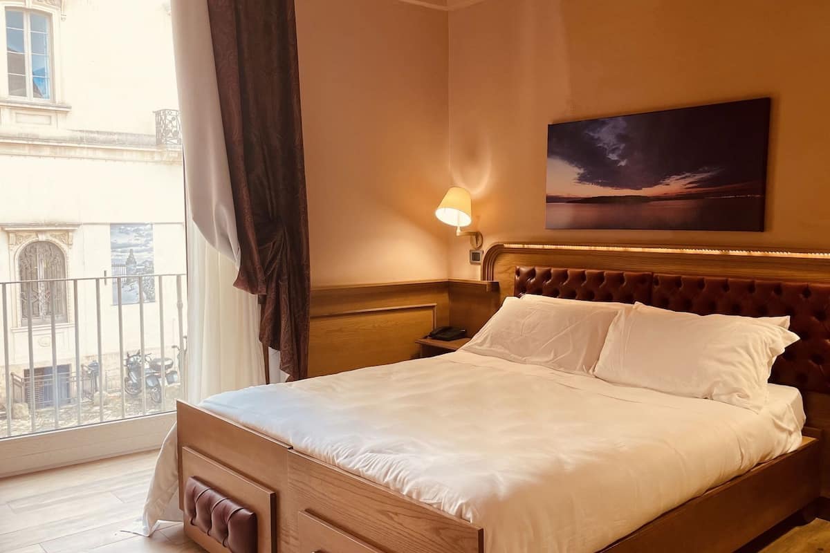 A hotel room with a large bed, a view of the city, and a painting on the wall.