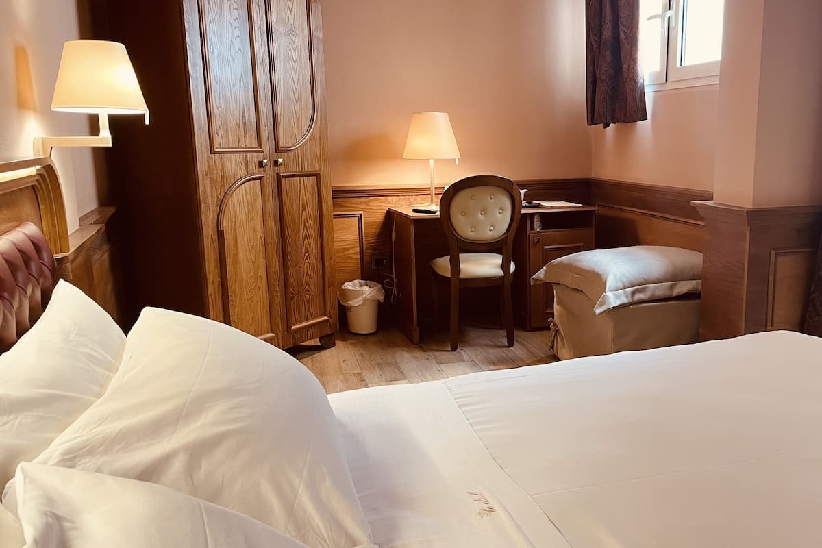 A hotel room with a bed, a desk, a chair, and a lamp.