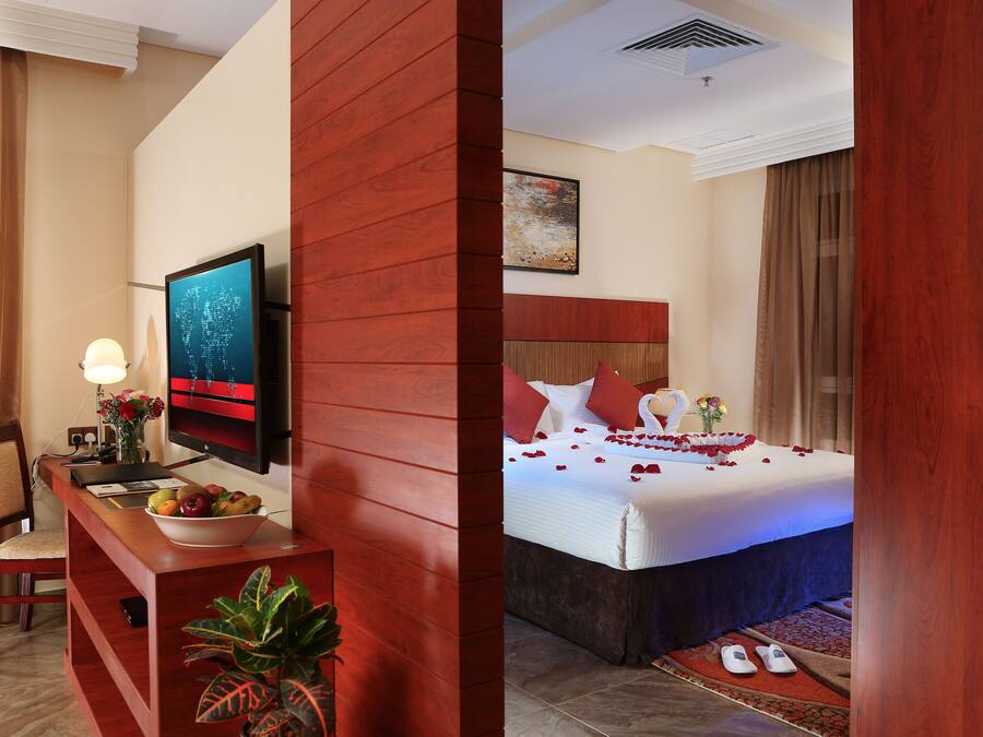 A hotel room with a desk, TV, and a bed with rose petals.