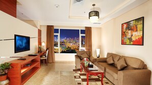 A modern living room with a television, sofa, coffee table, and a city view through large windows. - Best Western Plus Salmiya (Salmiya)