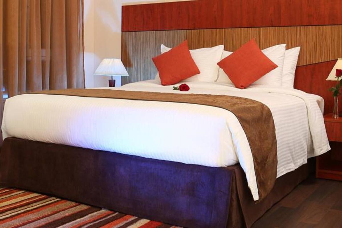 A hotel room with a large bed, a wooden headboard, two bedside tables with lamps, and a striped carpet.